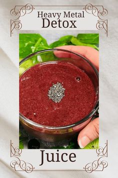 a hand holding a glass filled with red liquid next to lettuce and leaves