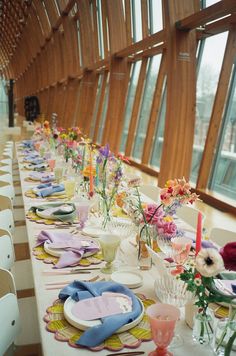 a long table is set with plates and flowers in vases on the tables, along with other place settings