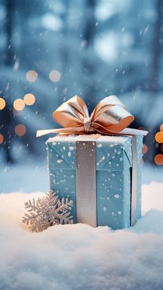 a blue gift box with a gold bow sitting in the snow