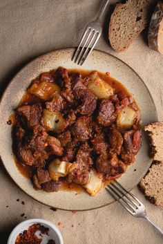 a white plate topped with meat and potatoes covered in gravy next to bread