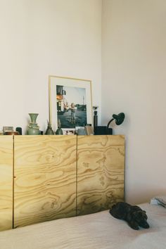 a wooden cabinet sitting on top of a bed next to a painting and pictures above it