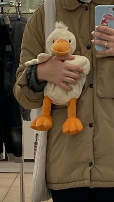 a woman holding a stuffed duck in her arms while wearing a face mask and coat