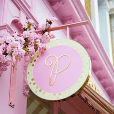 a pink and gold sign hanging from the side of a building with flowers in front of it