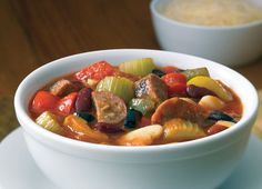 a white bowl filled with meat and vegetables on top of a table next to a cup