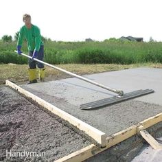 a man in green shirt and yellow boots working on cement with a large metal pole