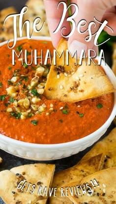 a hand dipping some tortilla chips into a bowl of red sauce and garnish