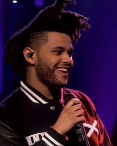 a man with dreadlocks on his head is smiling and holding a microphone in front of him