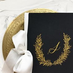 a black and gold wedding guest book with a white bow on it's side