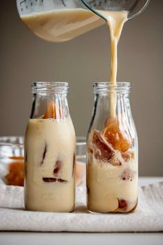 a person pouring orange juice into two glass jars filled with desserts and toppings