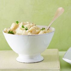 a white bowl filled with food sitting on top of a table next to a spoon