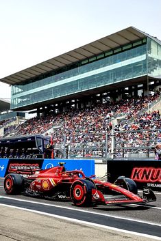 a red race car driving down a track in front of a large stadium filled with people