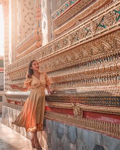 a woman leaning against a wall in front of an intricately decorated building with gold and red trim