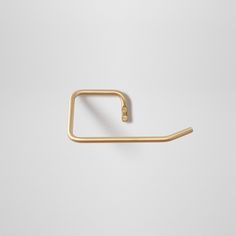 a gold metal hook on a white wall with the handle in the shape of a rectangle