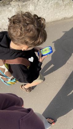 a little boy that is holding a cellphone in his hand and wearing a backpack