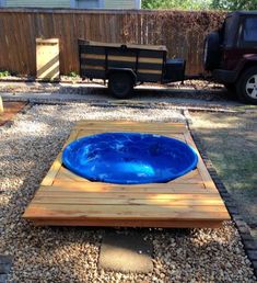 a blue pool in the middle of gravel next to a wooden deck and fenced yard