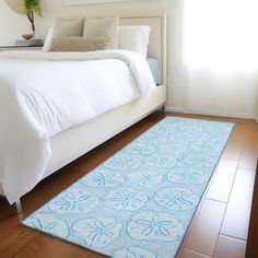 a white bed sitting next to a blue rug on top of a hard wood floor