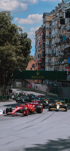 a group of racing cars driving down a race track in front of tall apartment buildings