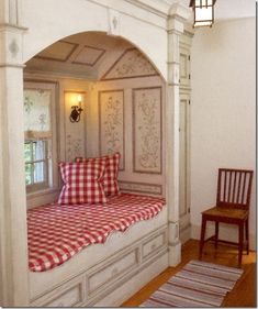 a room with a window seat and red checkered pillows on the cushioned bed