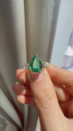 a woman's hand holding an emerald and diamond ring