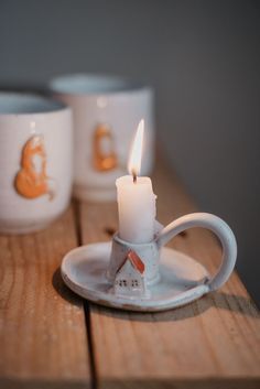 two coffee mugs sitting next to each other on a wooden table with a lit candle in the middle