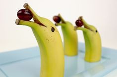 three bananas with faces drawn on them sitting on a blue tray and one banana has been cut in half