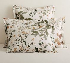 two pillow cases sitting next to each other on a white surface with flowers and leaves