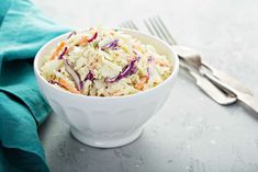 a white bowl filled with coleslaw on top of a table next to silverware