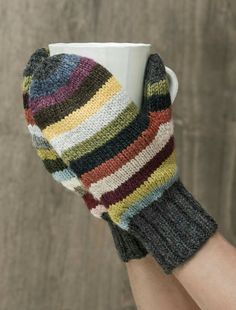 a woman's hand holding a coffee cup with multi - colored knitted mitts