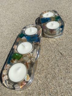 two glass candles are sitting on the sand