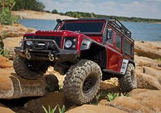 a red truck is on some rocks by the water