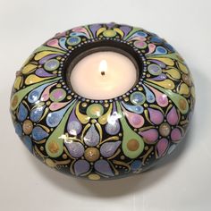 a colorful candle holder with a lit candle in the center on a white table top