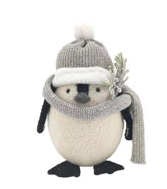 a stuffed penguin wearing a knitted hat and scarf with a pine branch in its beak