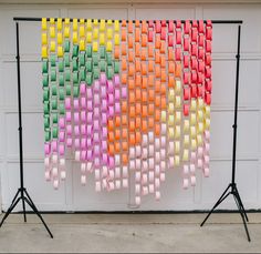 a multicolored wall hanging on the side of a garage door next to two black tripod stands