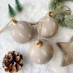 three ornaments are sitting in the snow next to pine cones