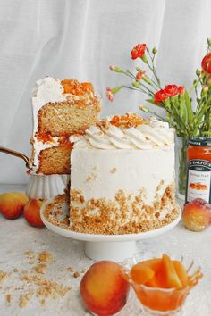 there is a cake on the table with peaches around it and some flowers in the background