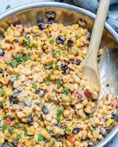 a skillet filled with mexican corn salad and topped with cilantro, black olives, red pepper, and green onions