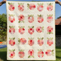 a person holding up a quilt with apples on it