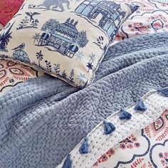 a bed covered in blue and white comforter next to a pillow with tassels on it