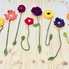 crocheted flowers are arranged on a white wooden surface with green stems and leaves