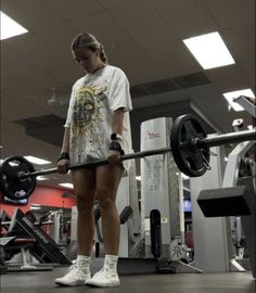 a woman standing in the middle of a gym holding a barbell