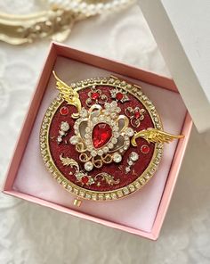 a red and gold brooch in a pink box