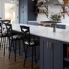 a kitchen with blue cabinets and white countertops has black chairs at the center of the island