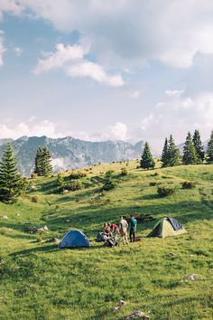 two tents set up on the side of a grassy hill with mountains in the background