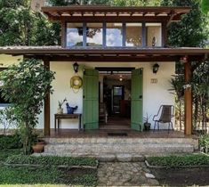 a small white house with green doors and steps leading up to the front door is surrounded by greenery