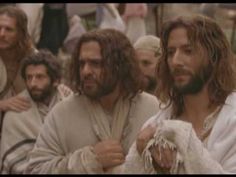 two men with long hair and beards standing in front of other men wearing white robes