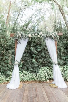 an outdoor ceremony setup with white drapes and flowers on the top, along with greenery