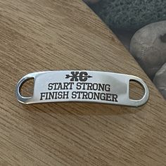 a metal keychain with the words start strong, finish strong on it next to some rocks