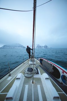 a man standing on the bow of a boat in the middle of the ocean with snow covered mountains behind him