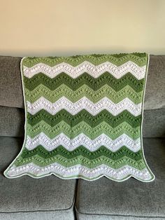 a green and white crocheted afghan sitting on top of a couch next to a pillow