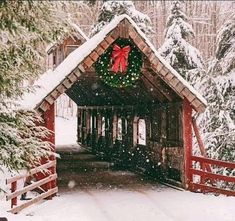 a covered bridge with wreaths and lights on it in the middle of snowy woods